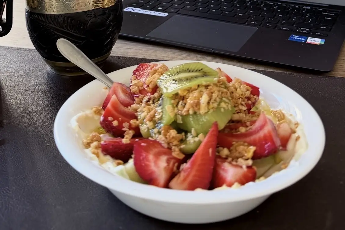 Bowl de yogur con frutillas, kiwi y granola sobre la mesa, junto a un mate
